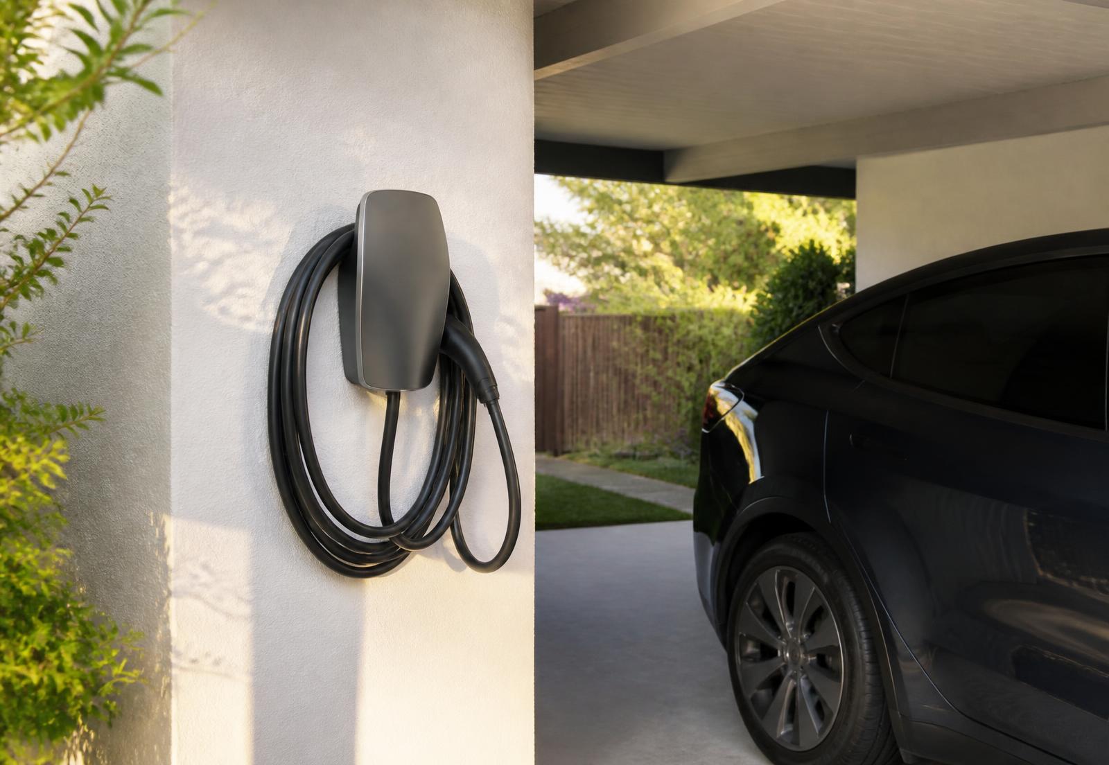 Wall-mounted Level 2 EV charger installed beside a home carport with an electric vehicle parked nearby